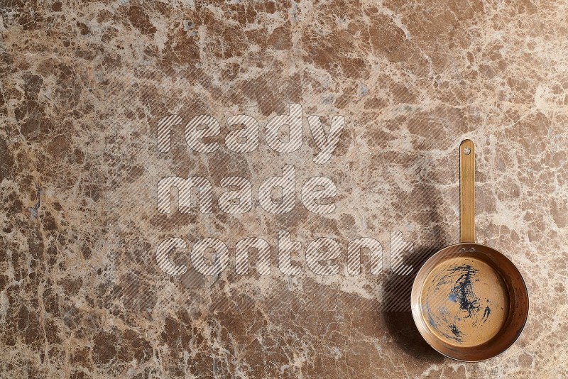 Top View Shot Of A Small Copper pan On beige Marble Flooring