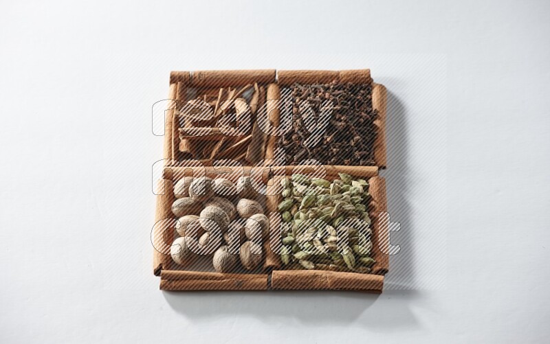 4 مربعات من أعواد القرفة ممتلئة بالهيل والقرفة والقرنفل وجوزة الطيب على أرضية بيضاء