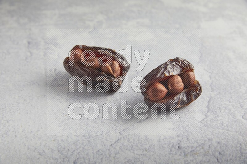 two hazelnuts stuffed madjoul dates on a light grey background