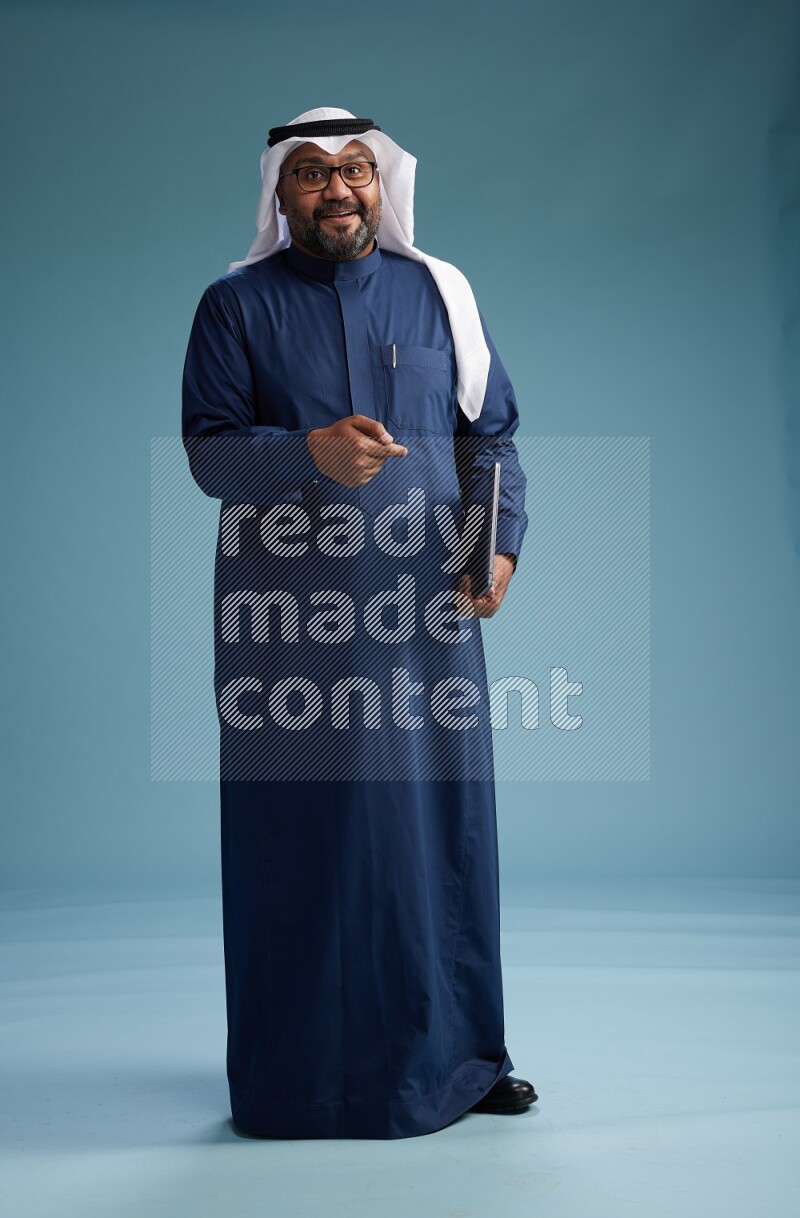 Saudi Man with shimag Standing working on laptop on blue background