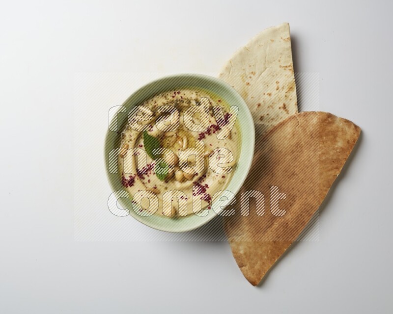 Hummus in a green plate garnished with zattar & sumak on a white background