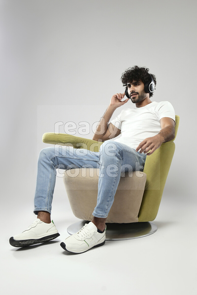 A man wearing casual sitting on a chair putting on headphones on white background