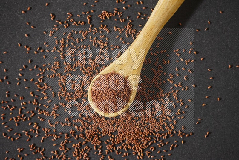 A wooden spoon full of garden cress seeds and seeds spread beside it on a black flooring