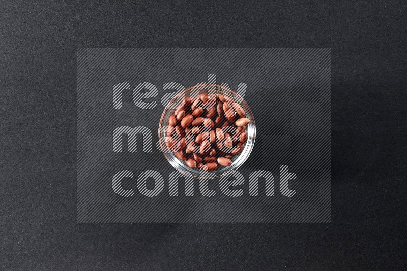 A glass bowl full of red skin peanuts on a black background in different angles