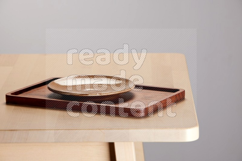 multi-colored pottery Plate placed on a rectangular wooden tray on the edge of wooden table
