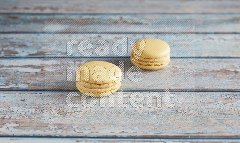 45º Shot of two Yellow Vanilla macarons on a light blue wooden background