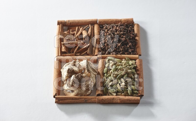 4 مربعات من أعواد القرفة ممتلئة بالهيل والقرفة والقرنفل والزنجبيل المجفف على أرضية بيضاء