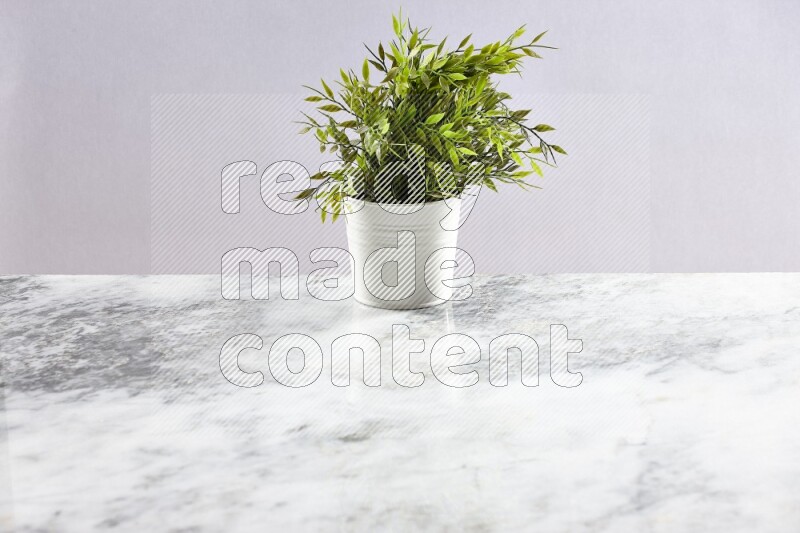 Green artificial plant in white pot on light grey marble background