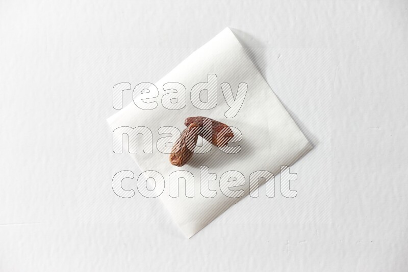 Two dried dates on a piece of paper on a white background in different angles
