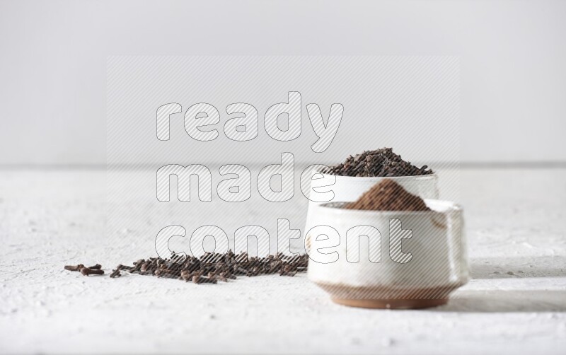 وعاءين من السيراميك بيج اللون، أحدهما مملوء بالقرنفل والآخر مملوء بالبودرة على أرضية بيضاء