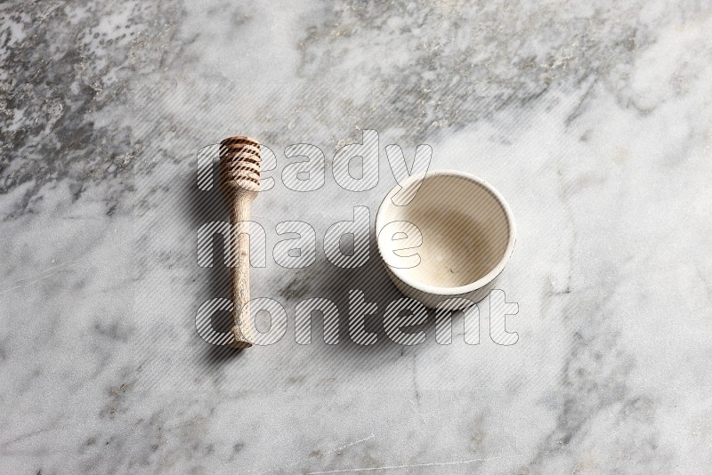 White Pottery bowl with wooden honey handle on the side with grey marble flooring, 65 degree angle