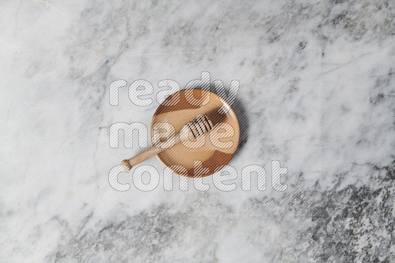 Multicolored Pottery Plate with wooden honey handle in it, on grey marble flooring, Top View