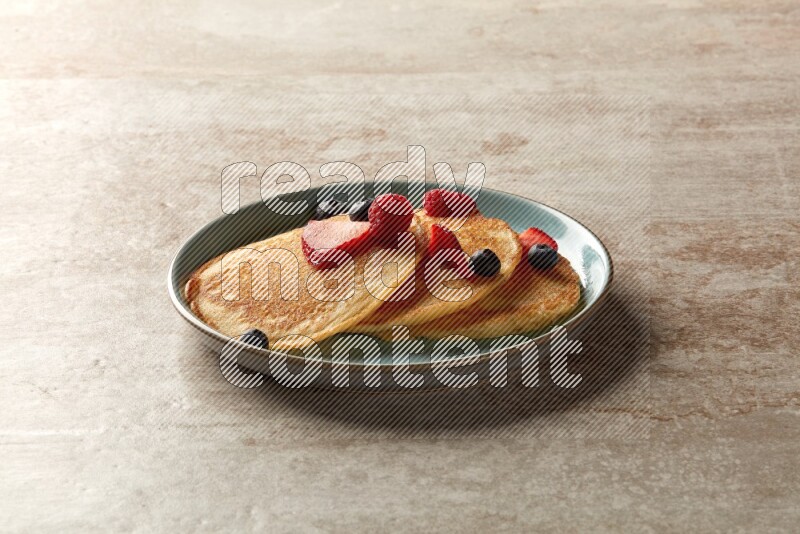 Three stacked mixed berries pancakes in a blue plate on beige background