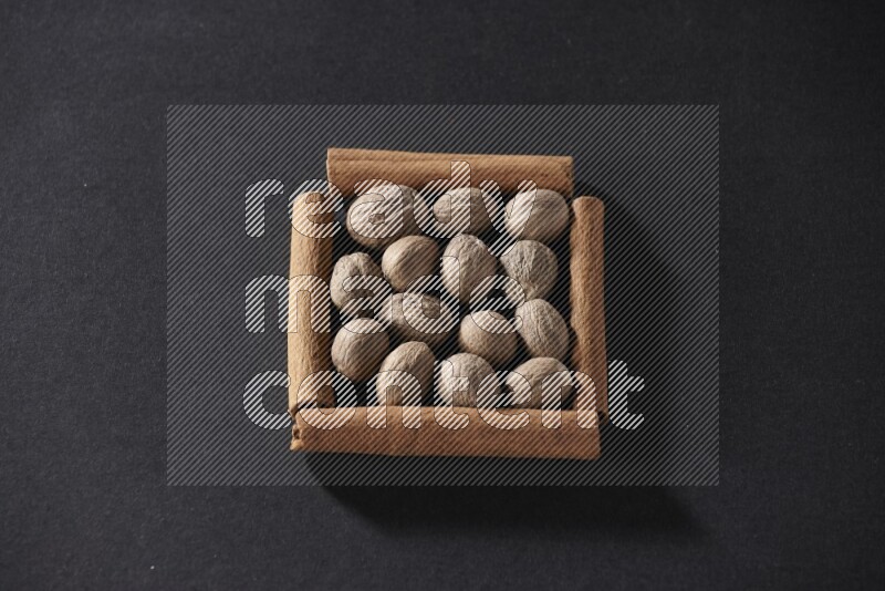 أربعة من أعواد القرفة مكونة شكل مربع بداخلها جوزة الطيب علي خلفية سوداء