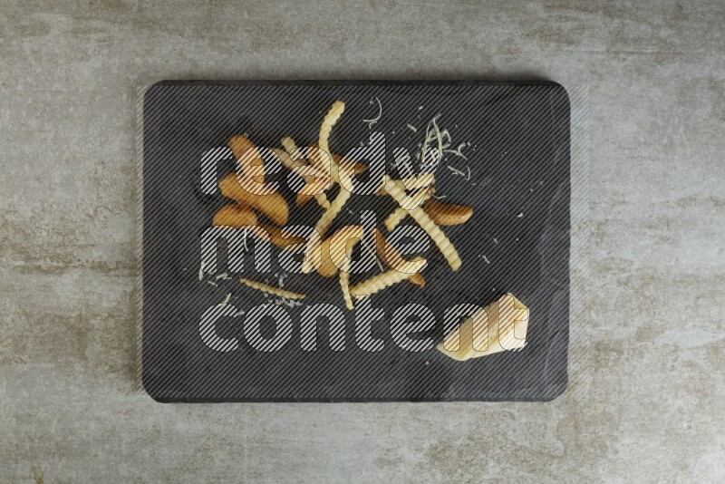 Mixed potatoes with cheese on a black stone serving platter on grey textured counter top