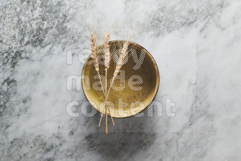 Wheat stalks on multicolored pottery oven plate on grey marble background