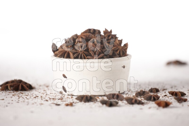 Star Anise in a white bowl and more of it sprinkled on white background