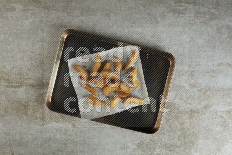 wedges potato on parchment paper in a black stainless steel rectangle tray on grey textured counter top