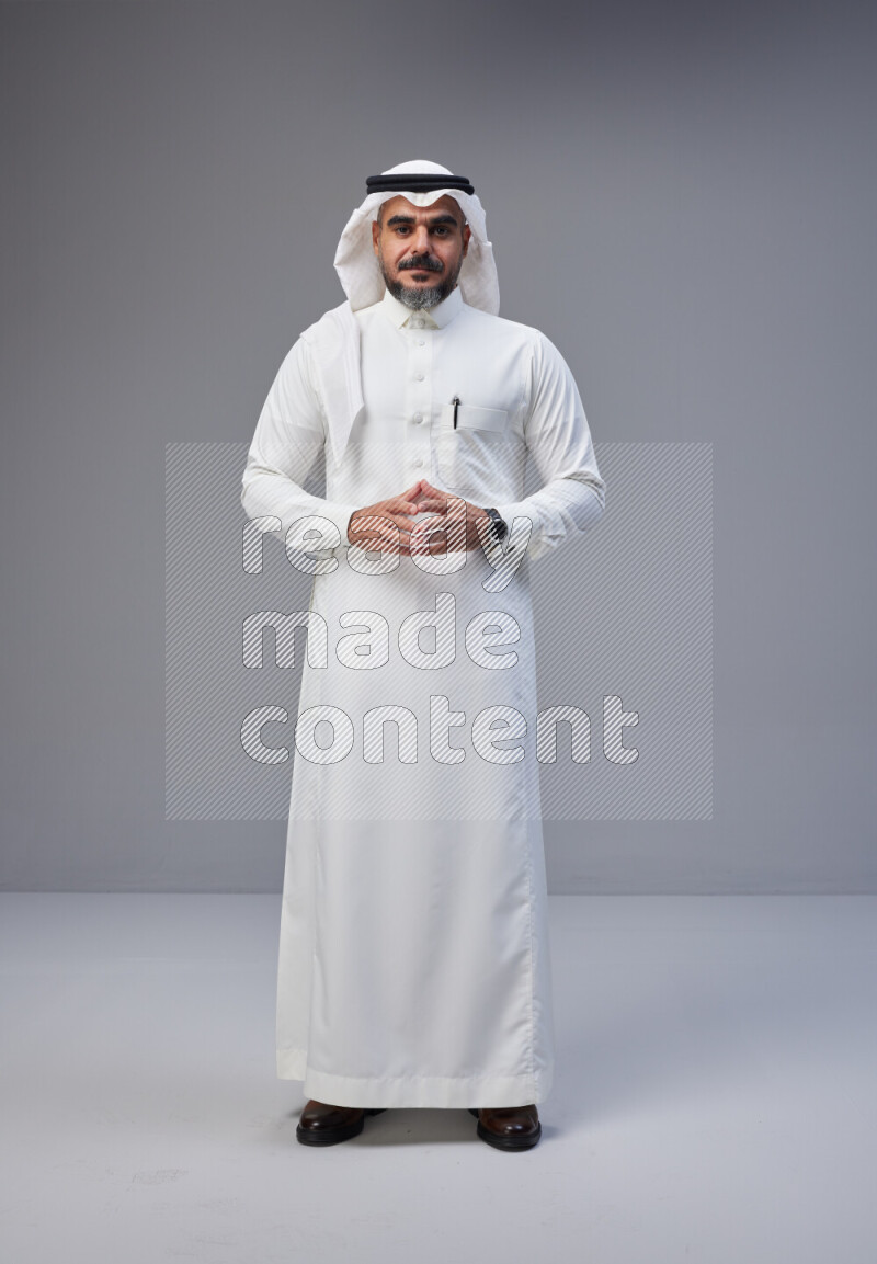 Saudi man Wearing Thob and white Shomag standing interacting with the camera on Gray background