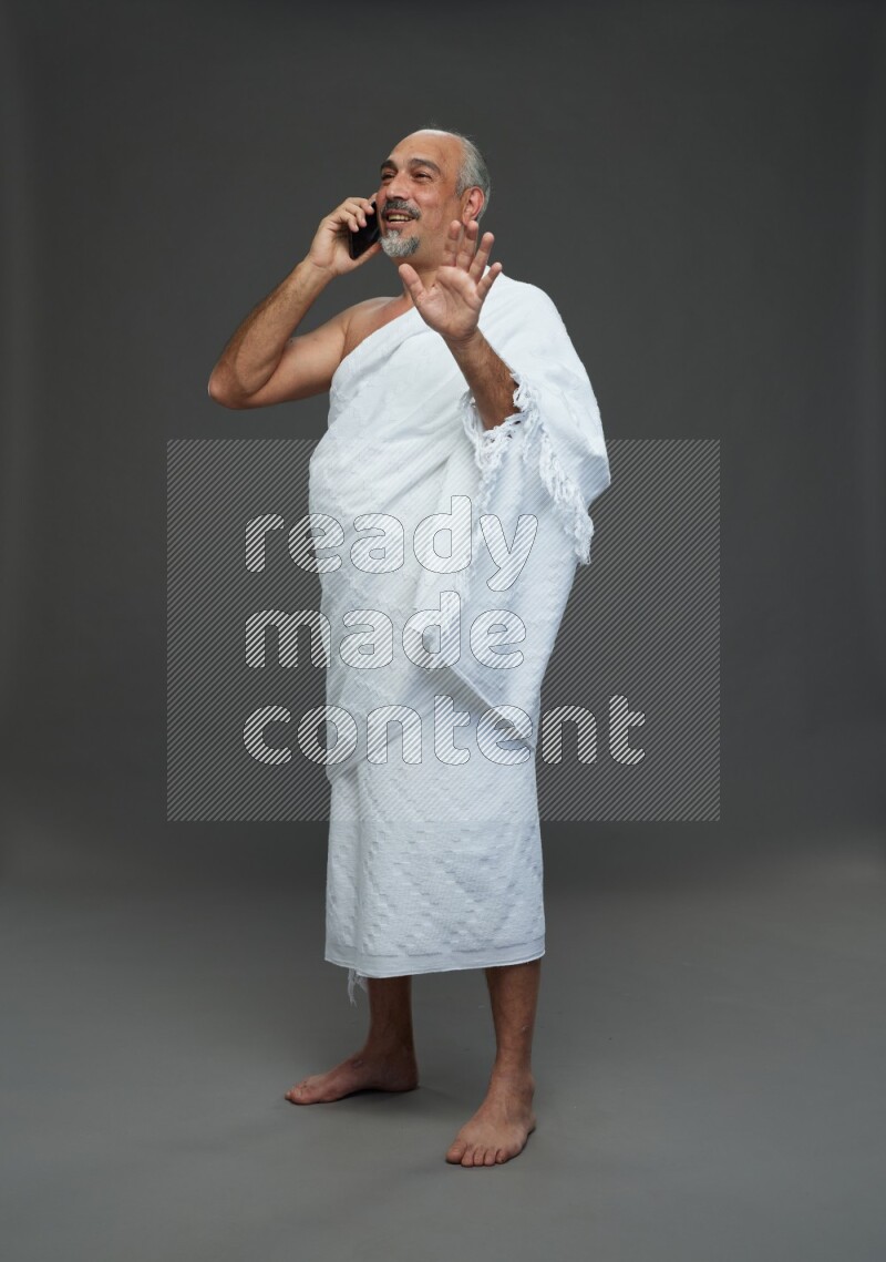 A man wearing Ehram Standing talking on phone on gray background