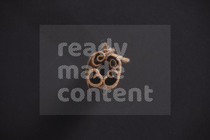 4 Cinnamon sticks stacked and bounded on black flooring