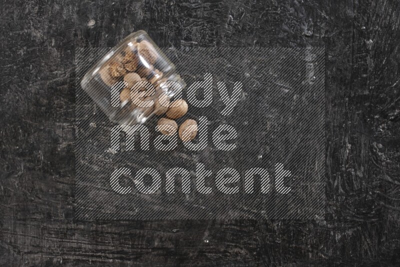 وعاء زجاجي ممتلئ بجوزة الطيب مقلوب وبعض الحبوب متناثرة على خلفية سوداء