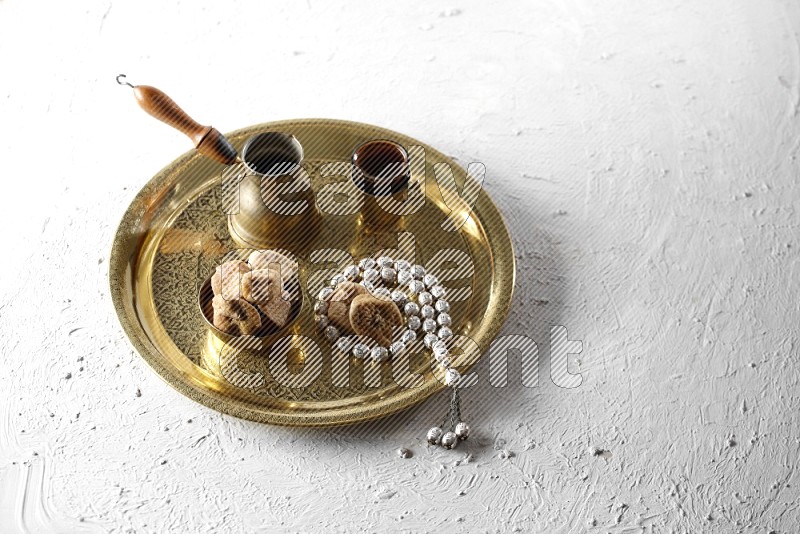 Dried figs in a metal bowl with coffee and prayer beads on a tray in a light setup