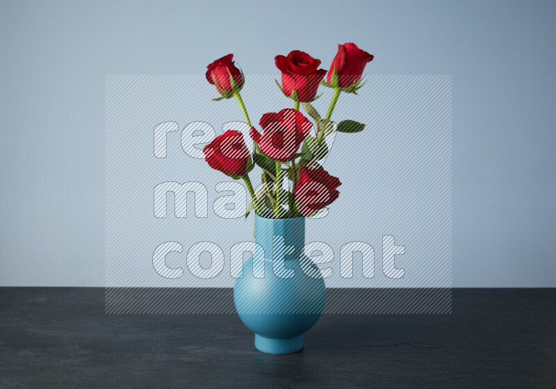 مجموعة من الورود الحمراء الزاهية في مزهرية زرقاء على خلفية من الرخام الأسود