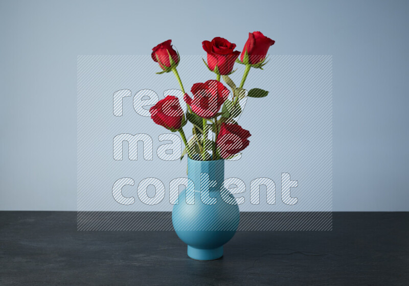 An arrangement of vivid red roses in a blue vase on black marble background