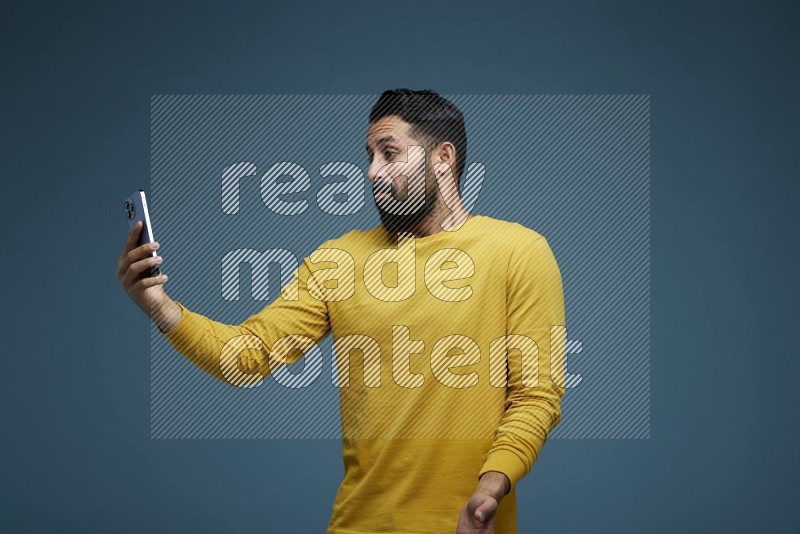 Man Taking a Selfie  in a blue background wearing a yellow shirt