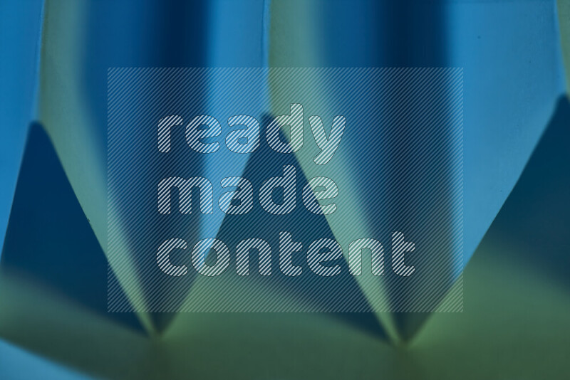 A close-up abstract image showing sharp geometric paper folds in green and blue gradients