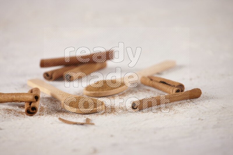 Two wooden spoons full of cinnamon powder with cinnamon sticks on white background