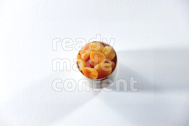 A beige ceramic bowl full of dried apricots on a white background in different angles