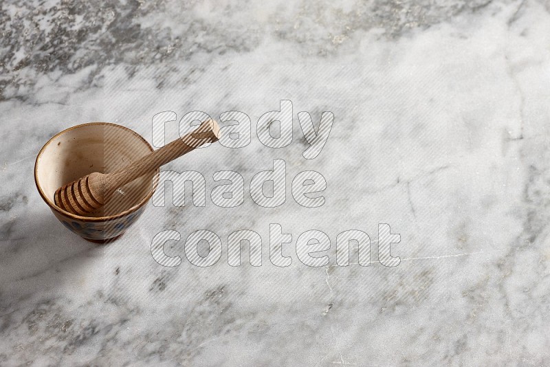 Decorative Pottery Bowl with wooden honey handle in it, on grey marble flooring, 65 degree angle