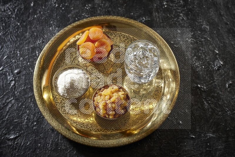 Dried fruits in metal bowls with water on a tray in dark setup