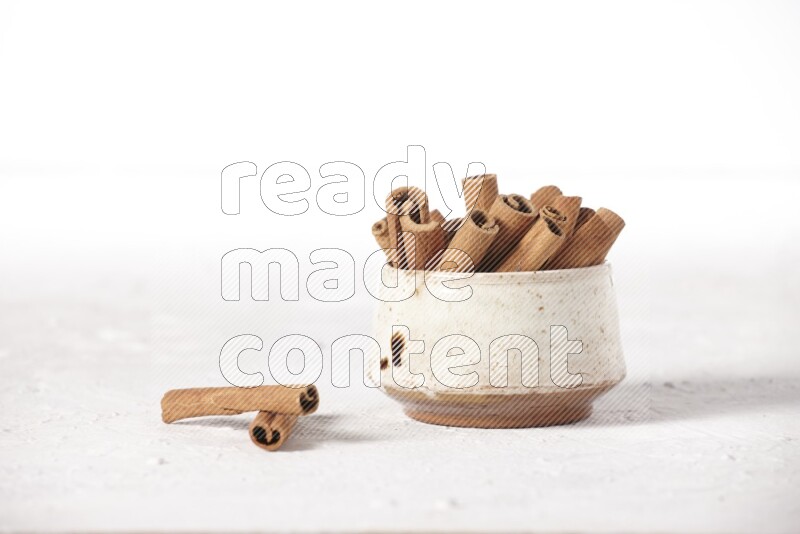 Cinnamon sticks in a beige bowl on a white background