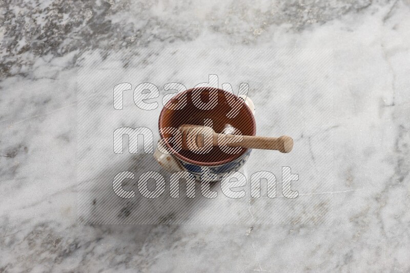 Decorative pottery pot with wooden honey dipper in it on grey marble background