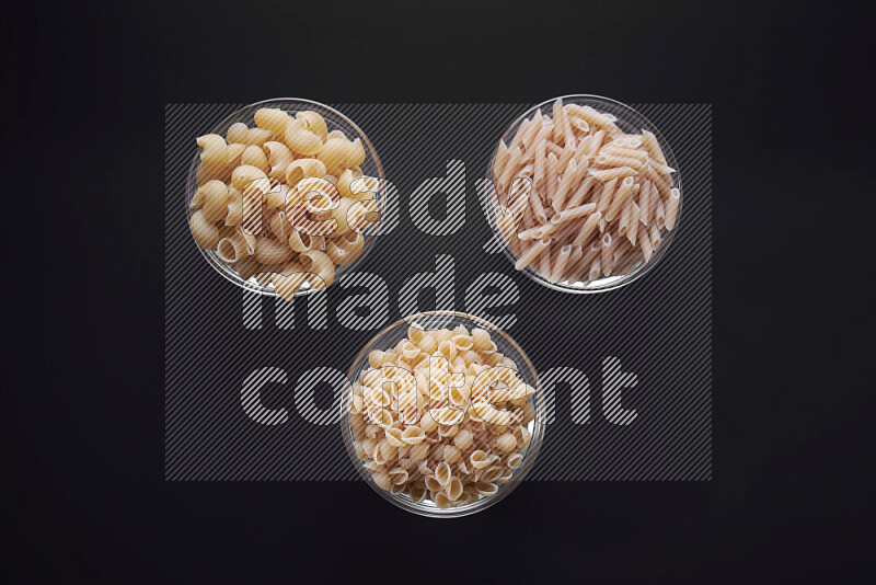 Different pasta types in glass bowls on black background