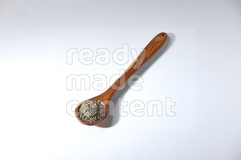 A wooden ladle full of cumin seeds on a white flooring