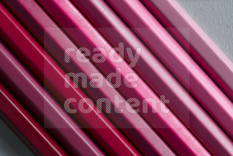 A collection of sharpened colored pencils arranged showcasing a gradient of pink hues on grey background