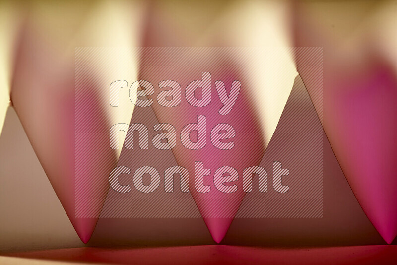 A close-up abstract image showing sharp geometric paper folds in pink gradients and warm tones