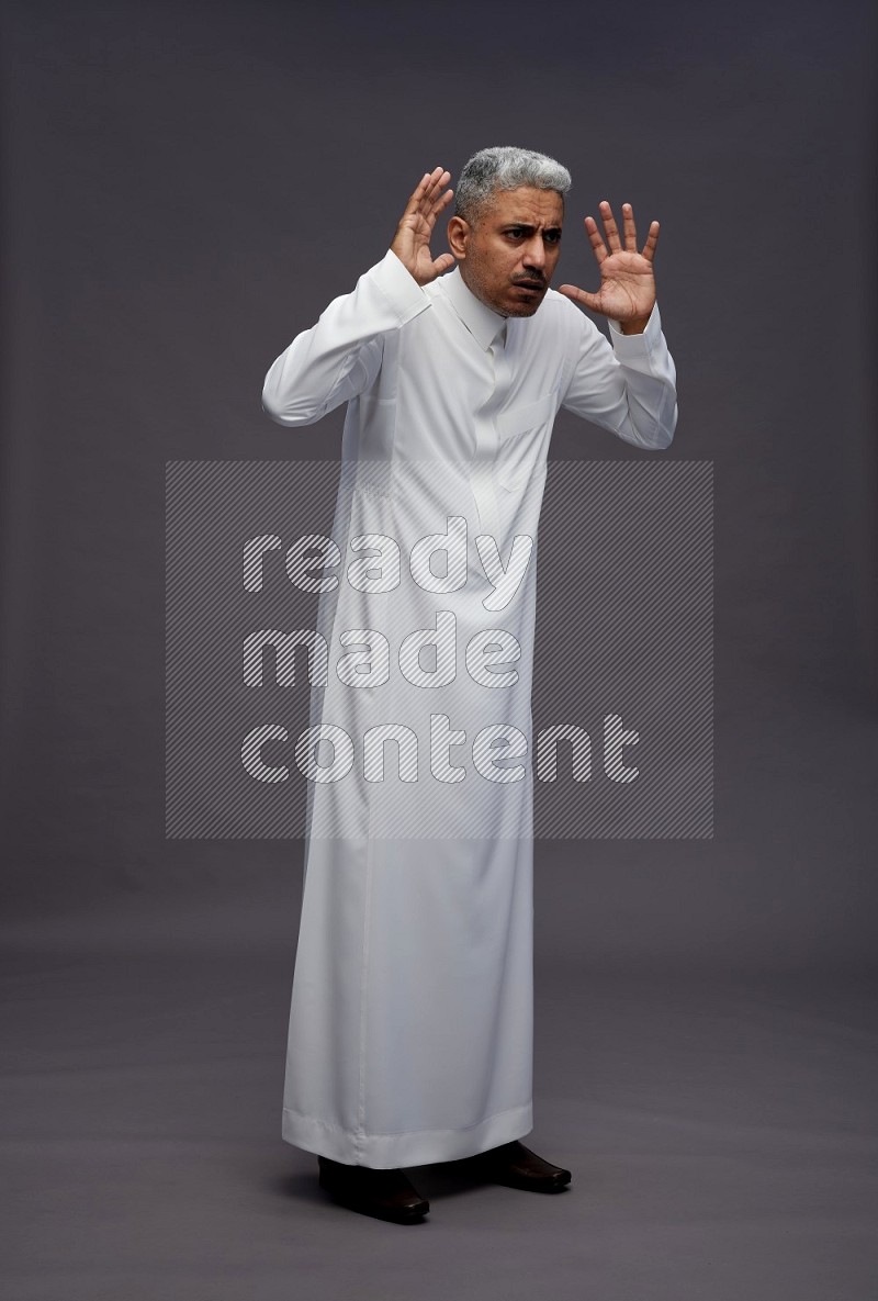 Saudi man wearing thob standing hands behind head on gray background