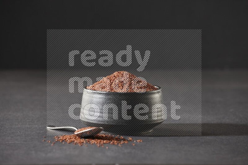 وعاء فخاري أسود ممتلئ ببذور حب الرشاد مع ملعقة معدنية ممتلئة بالبذور على أرضية سوداء