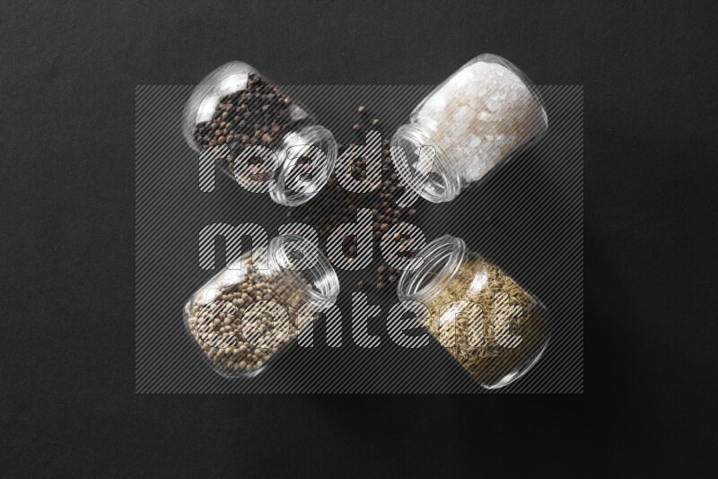 ملح وفلفل أسود وفلفل أبيض وكمون في أوعية زجاجية علي خلفية سوداء