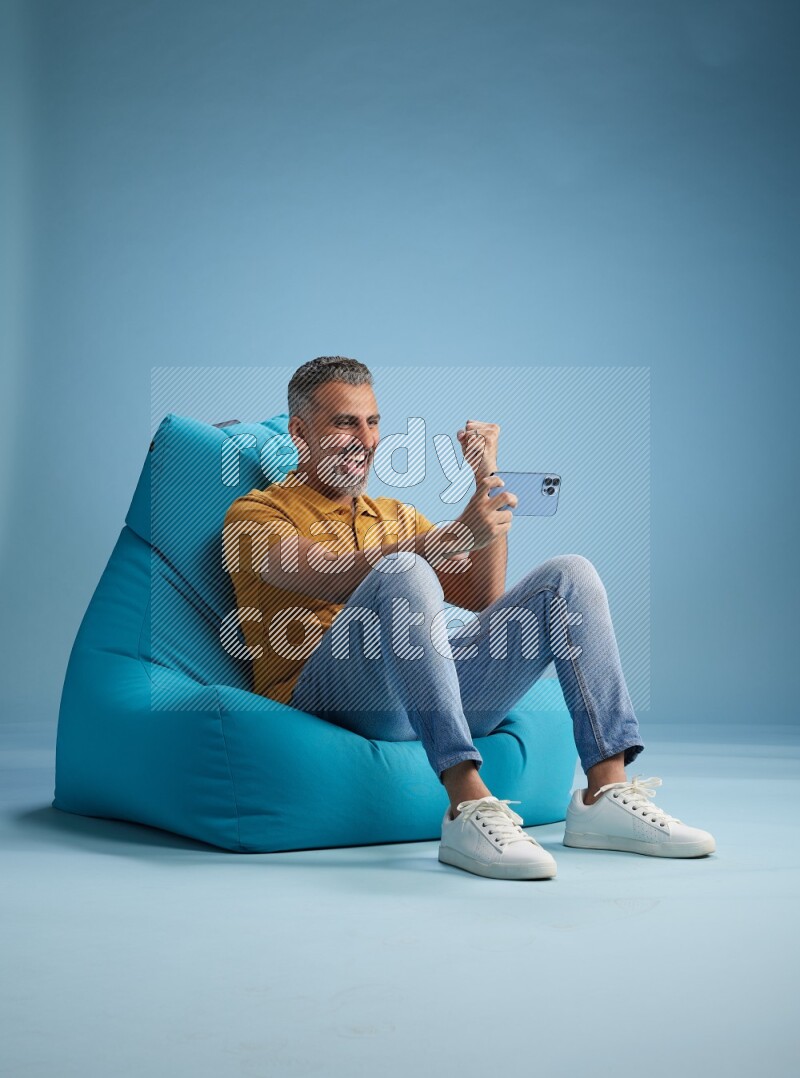 A man sitting on a blue beanbag and playing on phone