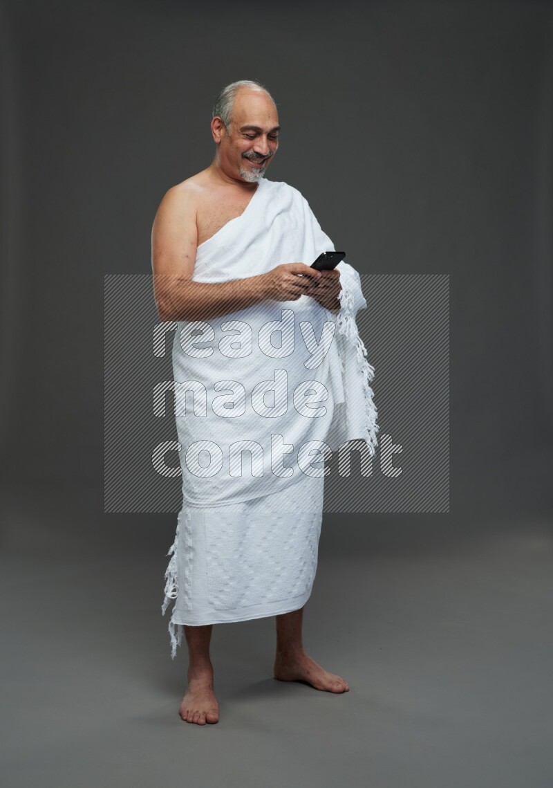 A man wearing Ehram Standing texting on phone on gray background