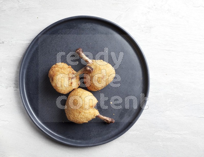 breaded drumstick on round dark grey pottery plate on grey textured countertop