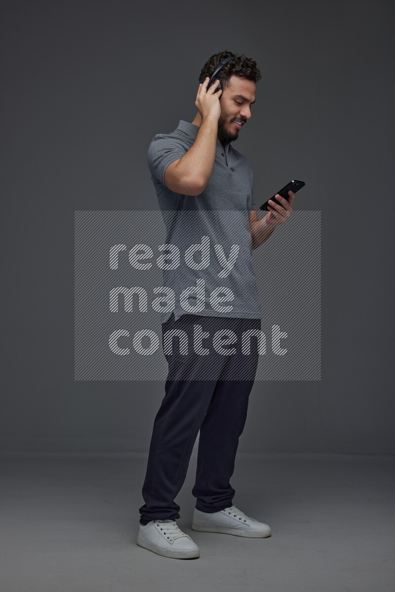 A man wearing casual and using his phone and headphone eye level on a gray background
