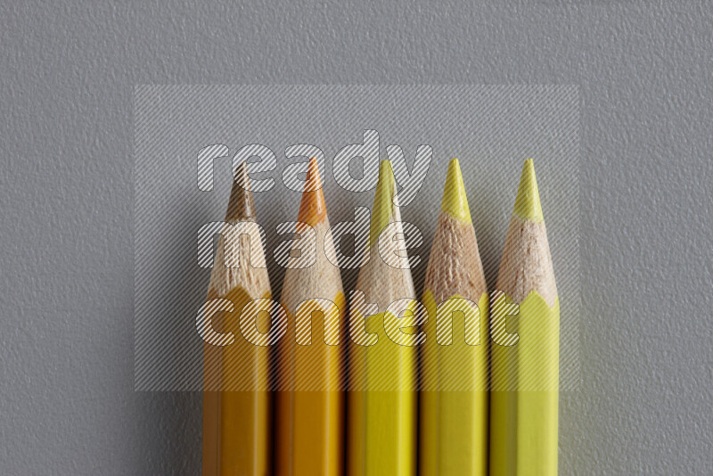A collection of sharpened colored pencils arranged showcasing a gradient of yellow and orange hues on grey background