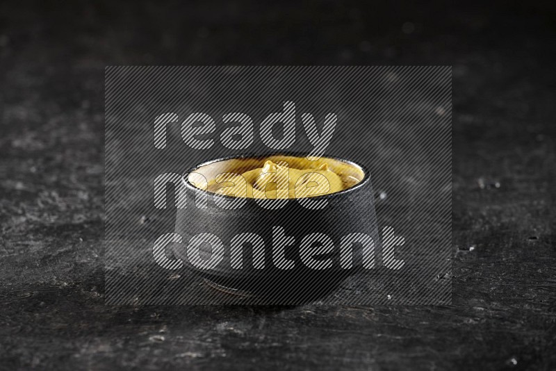 A black pottery bowl full of mustard paste on textured black flooring
